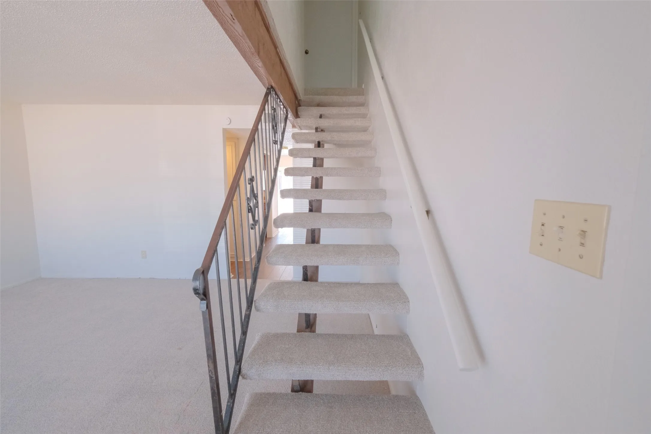 Carpeted staircase with an ornamental metal railing and wood-finish beam