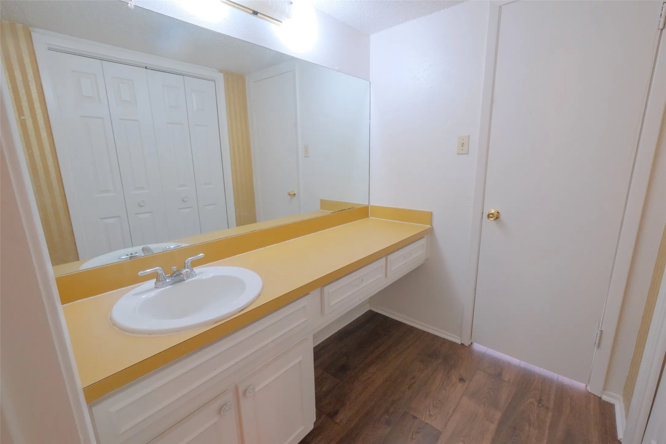 Vanity area featuring a single basin sink, a large mirror, a laminate countertop, white cabinetry with storage, and wood-finish flooring