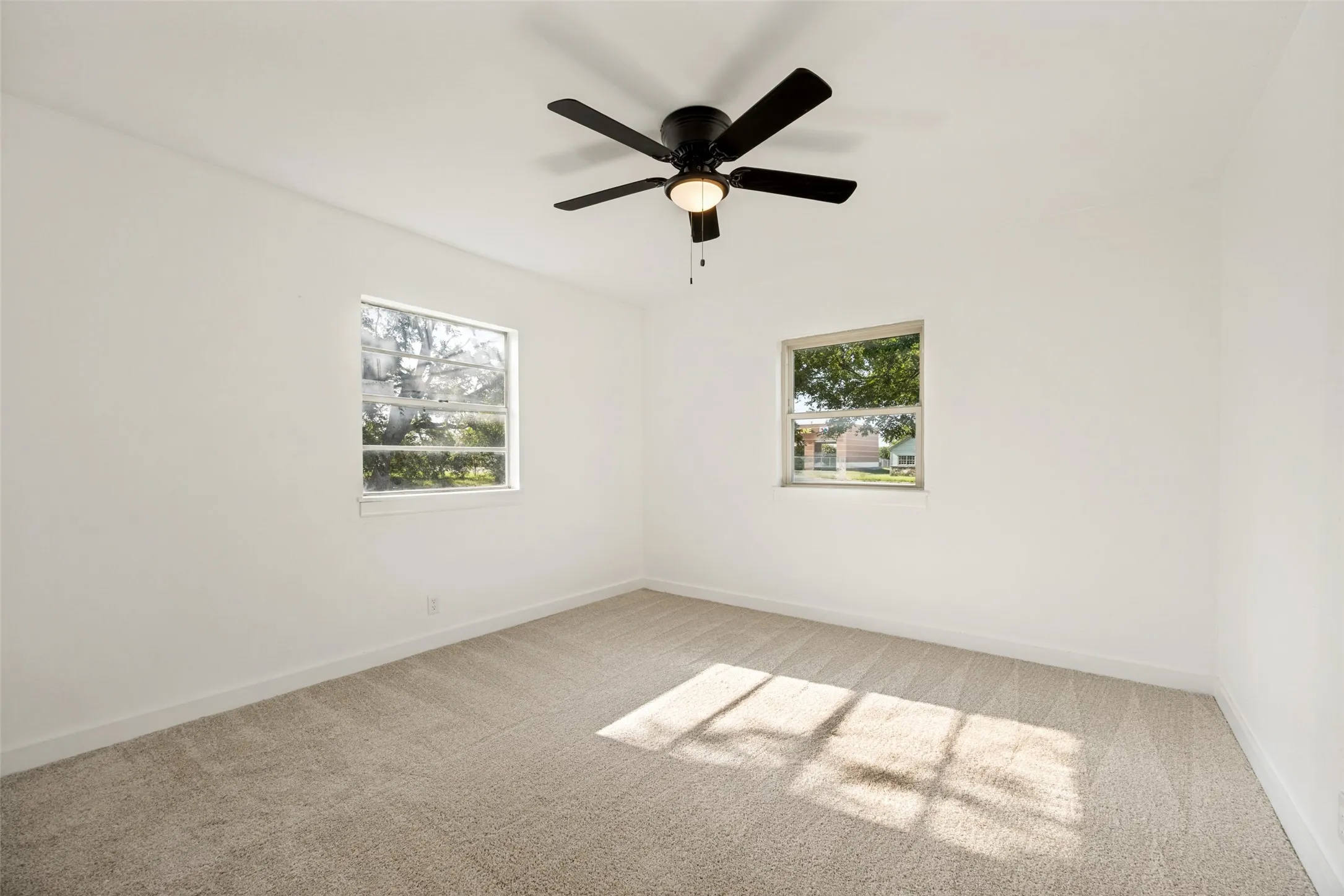 Spacious interior room featuring light-colored carpeting, white wall finishes, and a contemporary black ceiling fan with integrated lighting