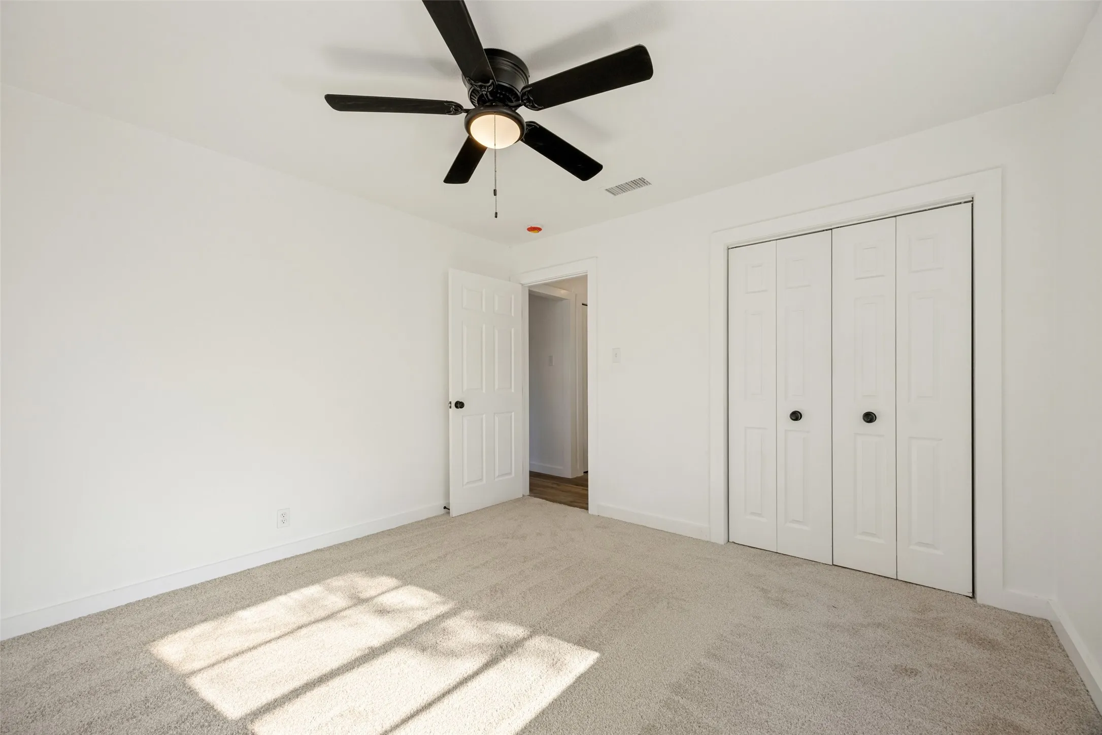 Carpeted room with a black ceiling fan, white bi-fold closet doors, and white walls