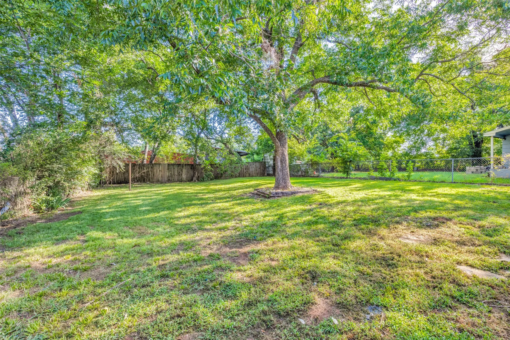 Expansive green lawn with mature trees and partial wood fencing