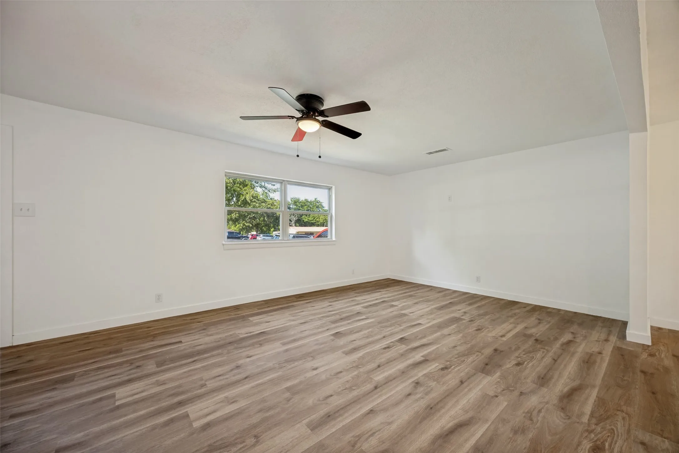 Spacious room featuring wood-finish flooring and a contemporary ceiling fan