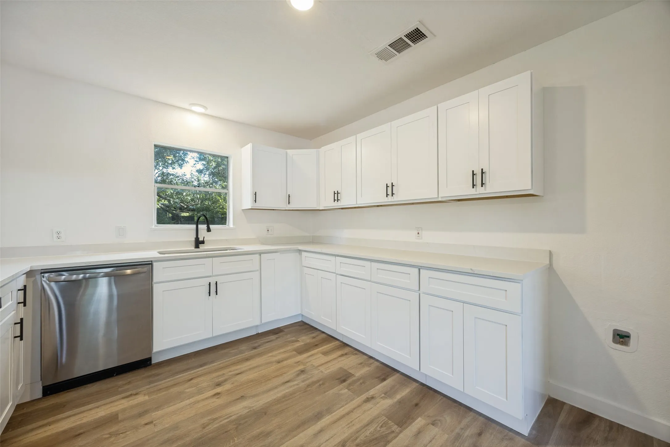 Kitchen featuring wood-finish flooring, white cabinetry with matte black hardware, light-toned countertops, and a stainless steel dishwasher