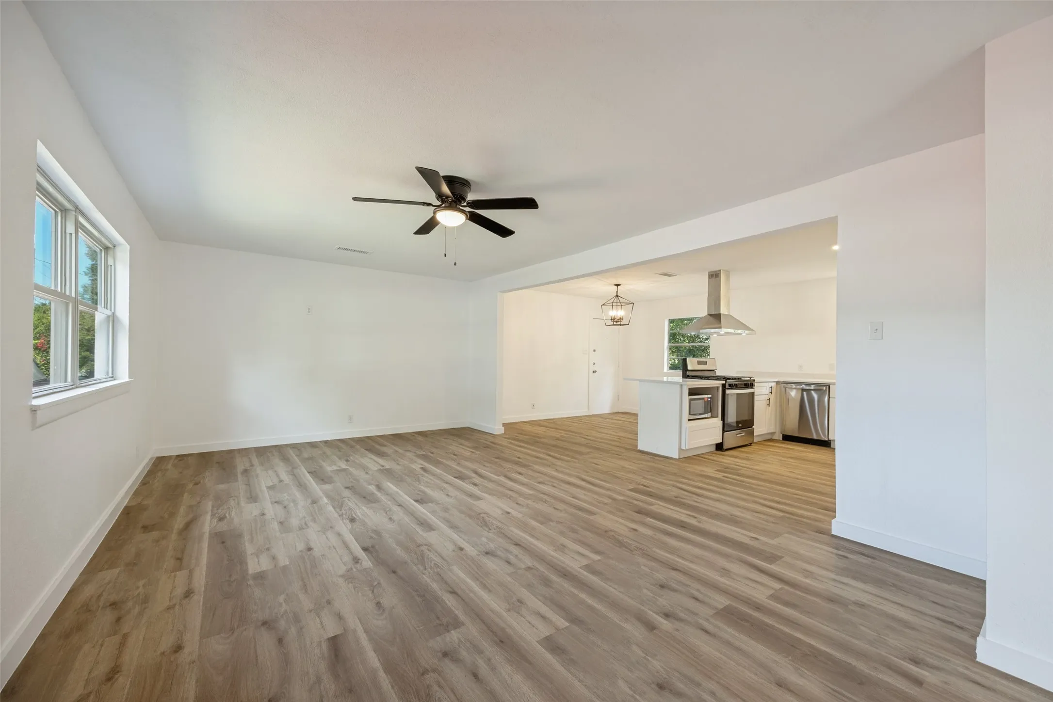 Spacious room featuring wood-finish flooring, white walls, and a ceiling fan