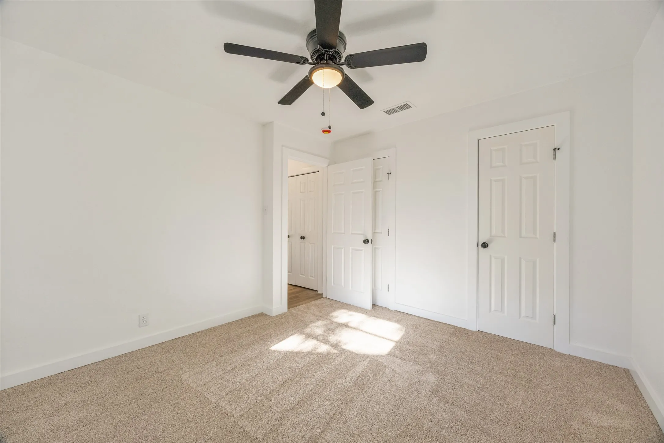 Interior room featuring a black ceiling fan, light-colored carpet flooring, white walls, white baseboards, and two white panel doors with black hardware