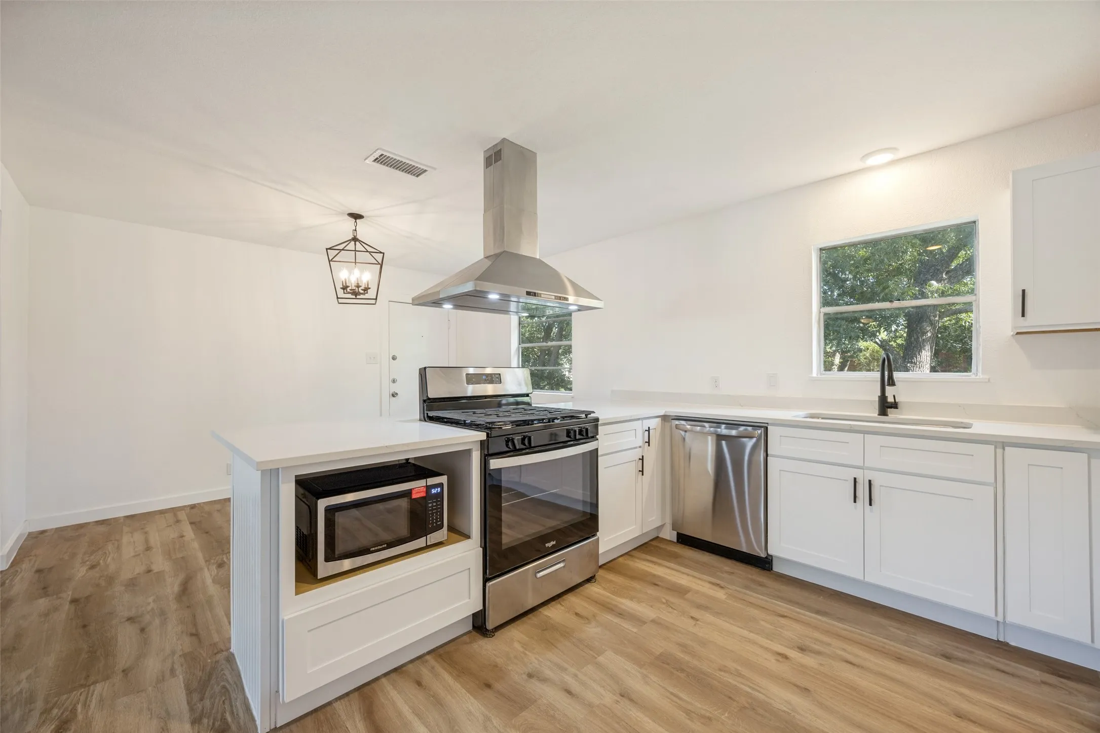 Modern kitchen featuring white cabinetry, light countertops, wood-finish flooring, stainless steel appliances, and a matte black faucet
