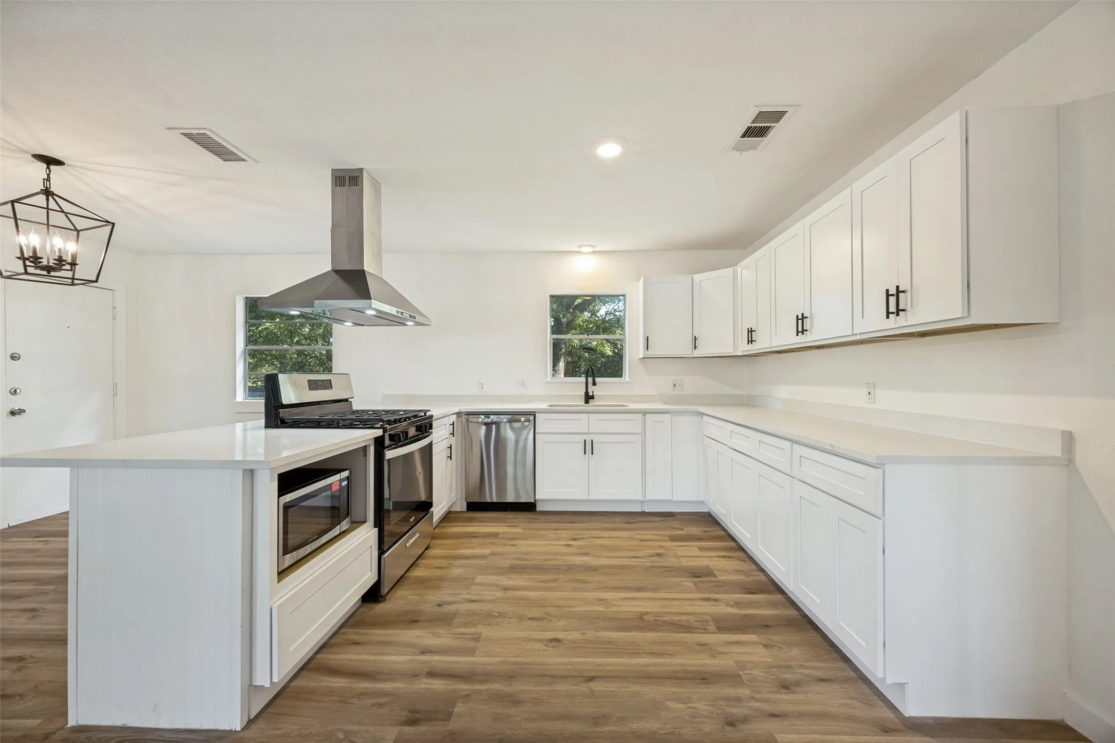 Modern kitchen featuring white cabinetry, light-colored countertops, stainless steel appliances, and wood-finish flooring