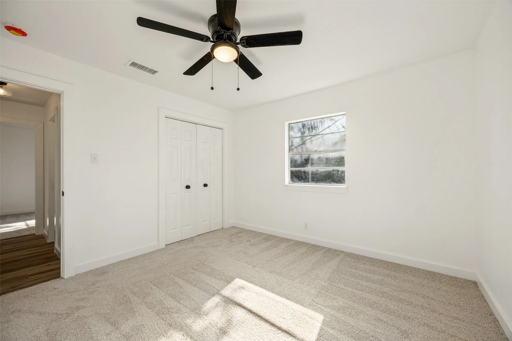 Carpeted room featuring a ceiling fan with integrated lighting, a window with white trim, and bi-fold closet doors with dark hardware
