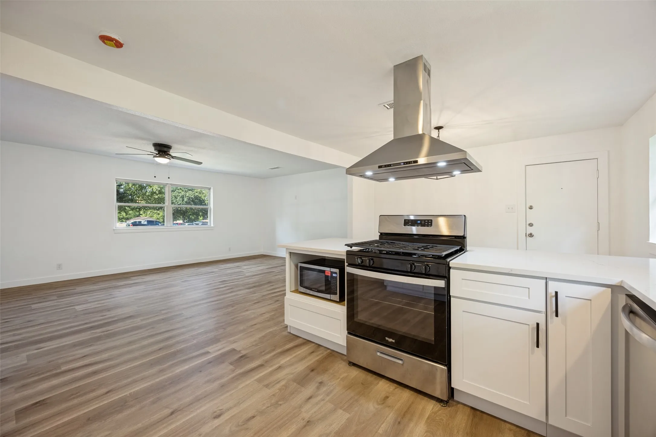 Open-concept kitchen and living area featuring wood-finish flooring, white cabinetry, a stainless steel range with a coordinating hood, and a ceiling fan in the living space