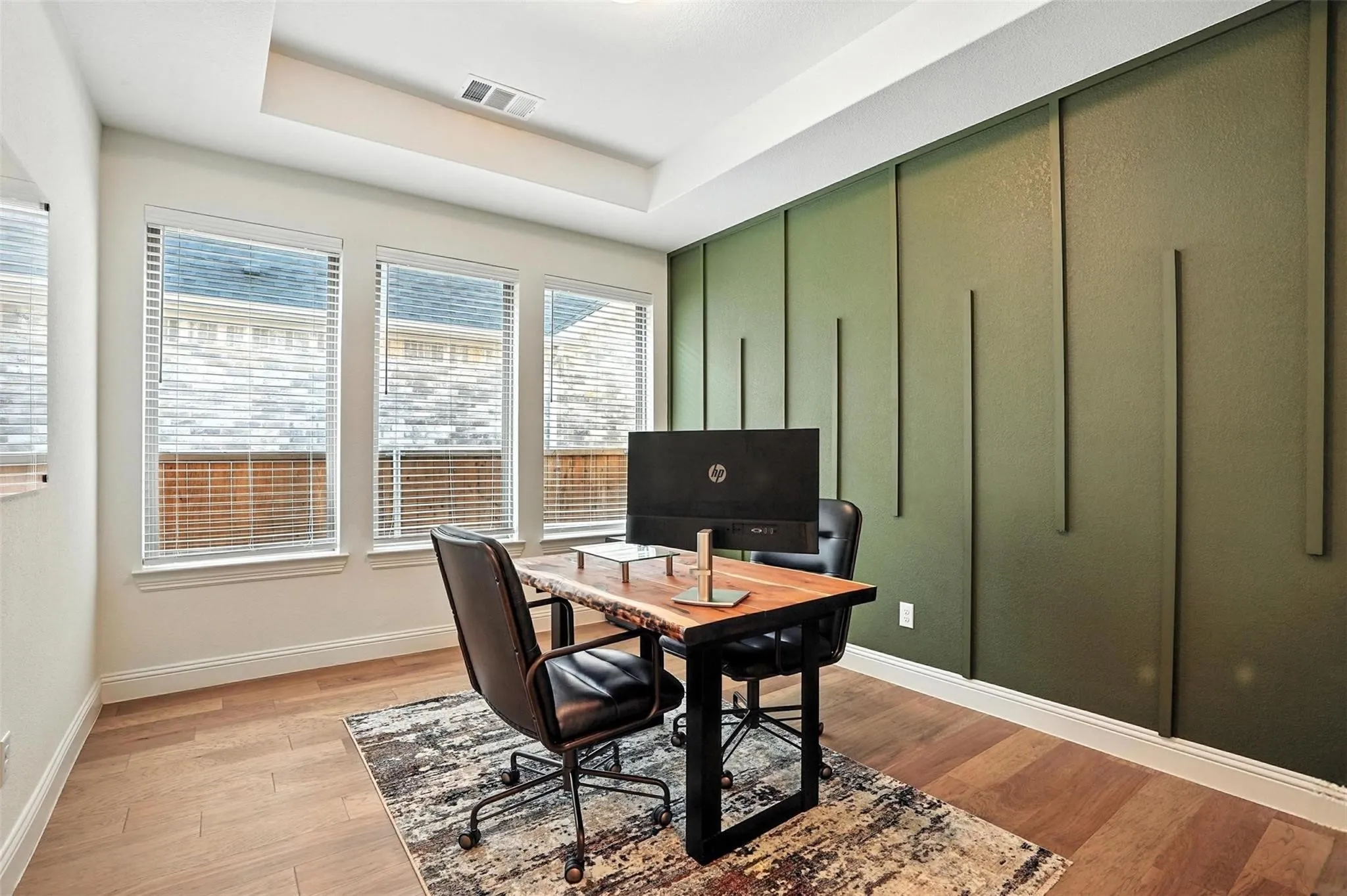 Office area featuring light wood finished floors, a tray ceiling, and a decorative wall