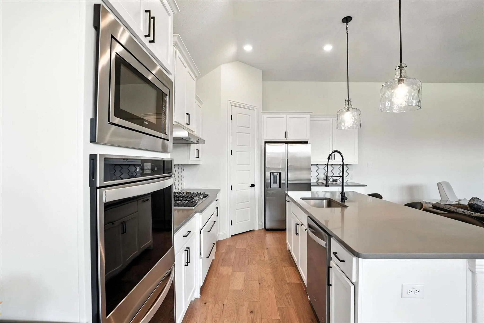 Kitchen with dark countertops, light wood finished floors, a center island with sink, appliances with stainless steel finishes, and recessed lighting