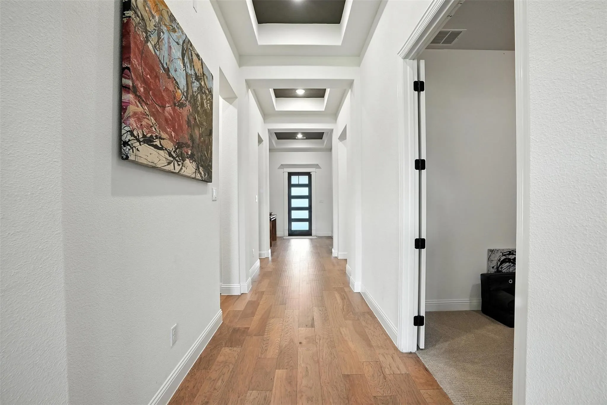 Hallway with light wood-type flooring, a tray ceiling, and a textured wall