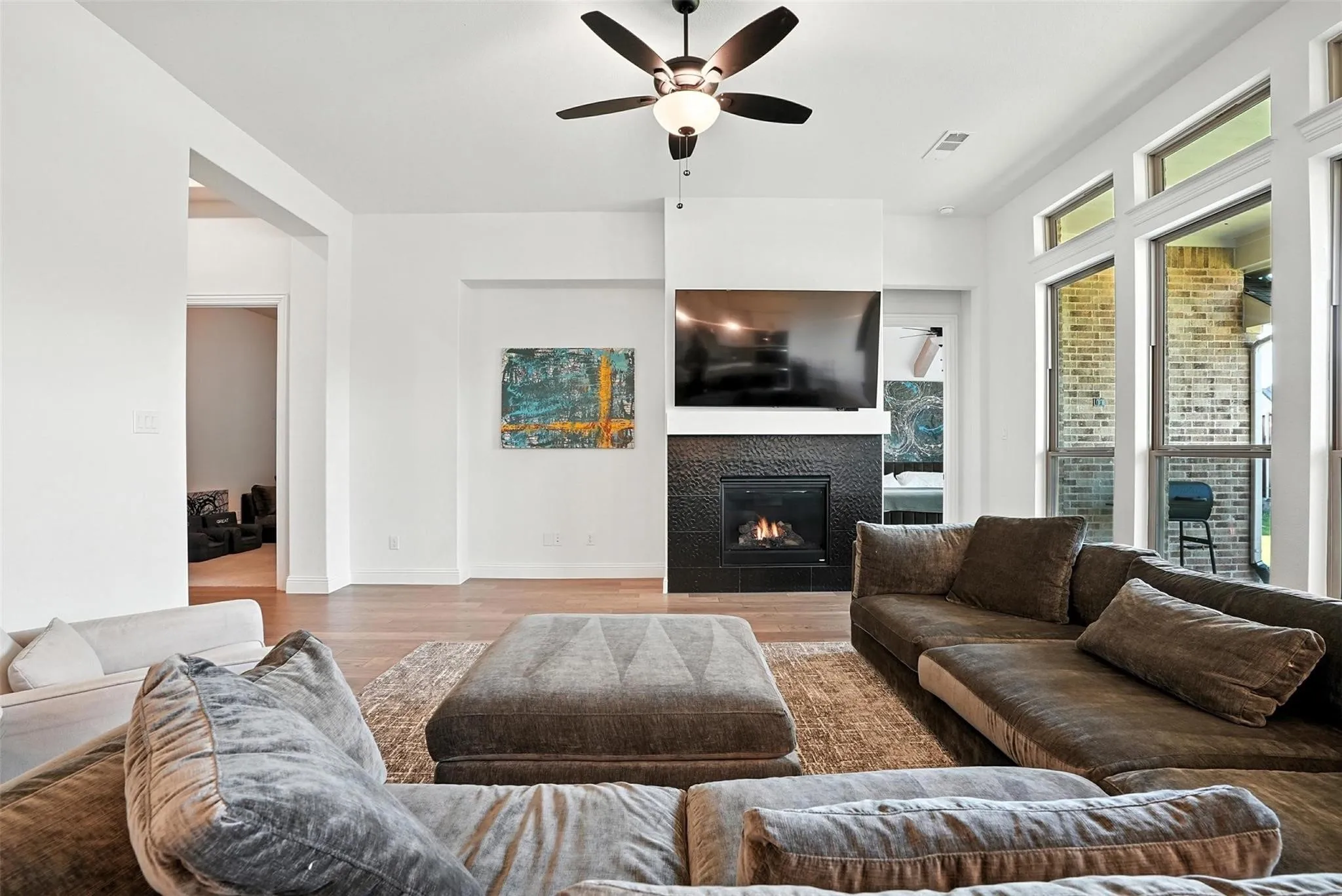 Living room with a ceiling fan, a glass covered fireplace, and wood finished floors