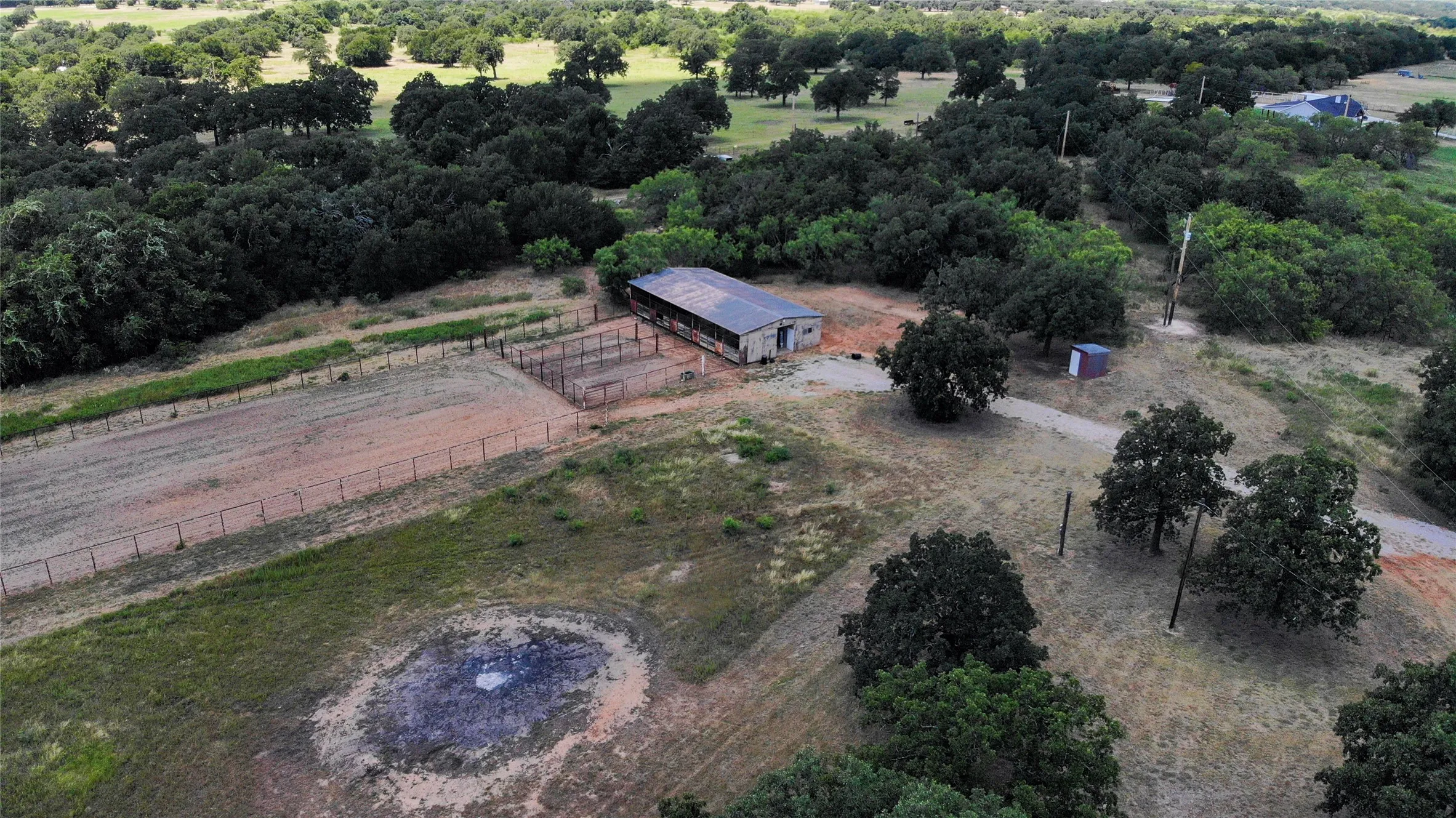 Expansive acreage featuring a large outbuilding with a metal roof, an arena with perimeter fencing, a gravel driveway, and numerous mature trees