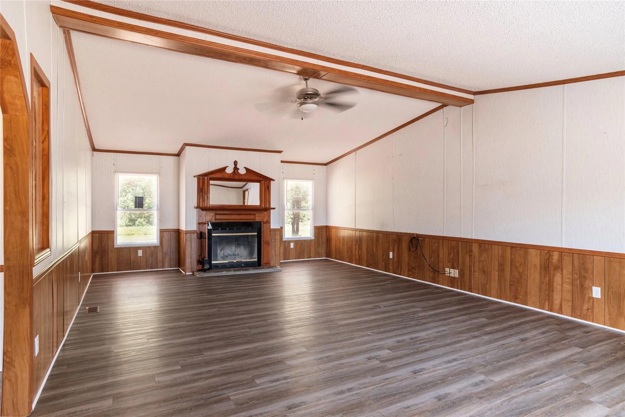 Spacious living area featuring wood-finish flooring, a decorative fireplace with an ornate wood mantel, and multiple windows