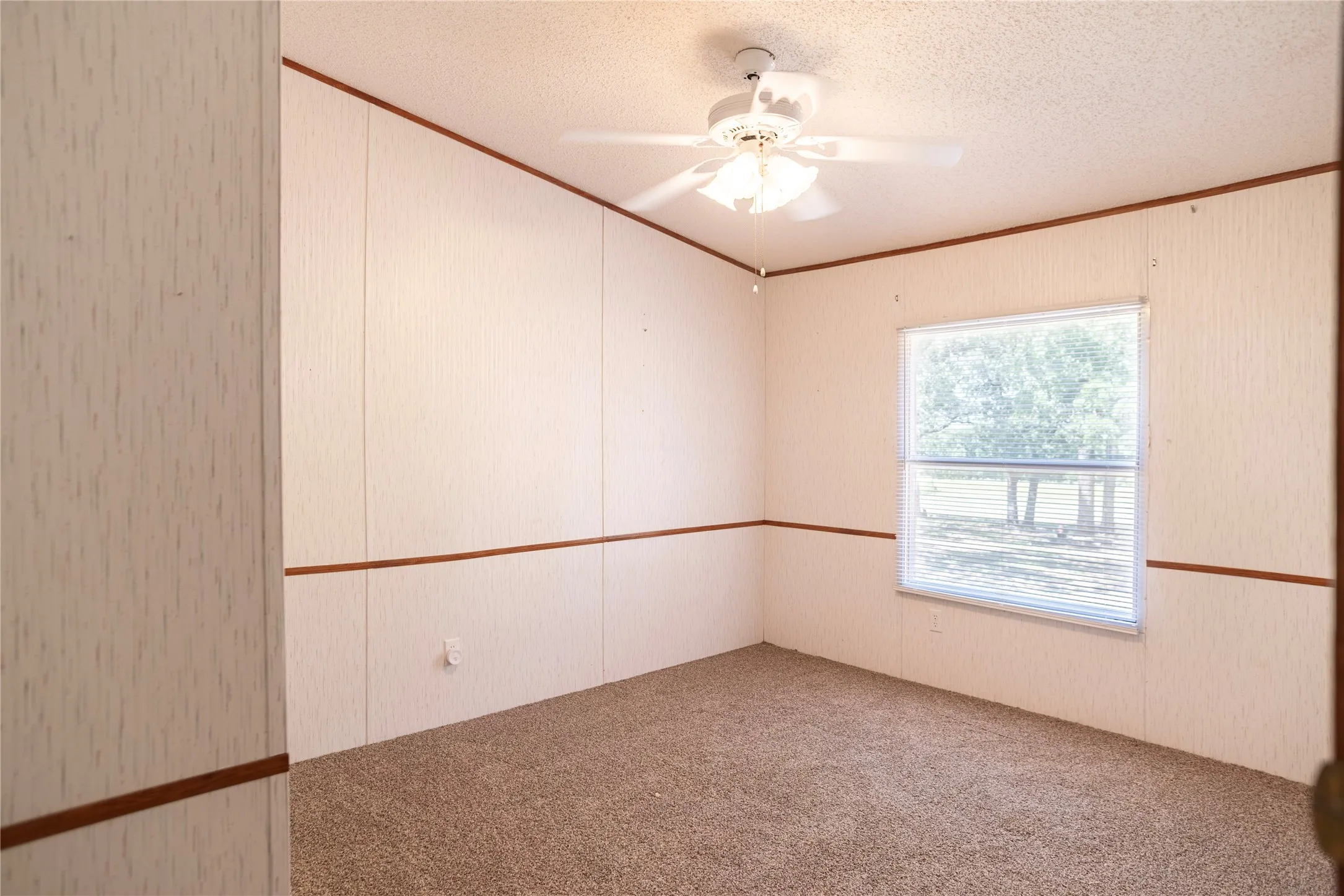 Interior room featuring light-colored panel walls with wood trim accents, a textured ceiling, and a ceiling fan