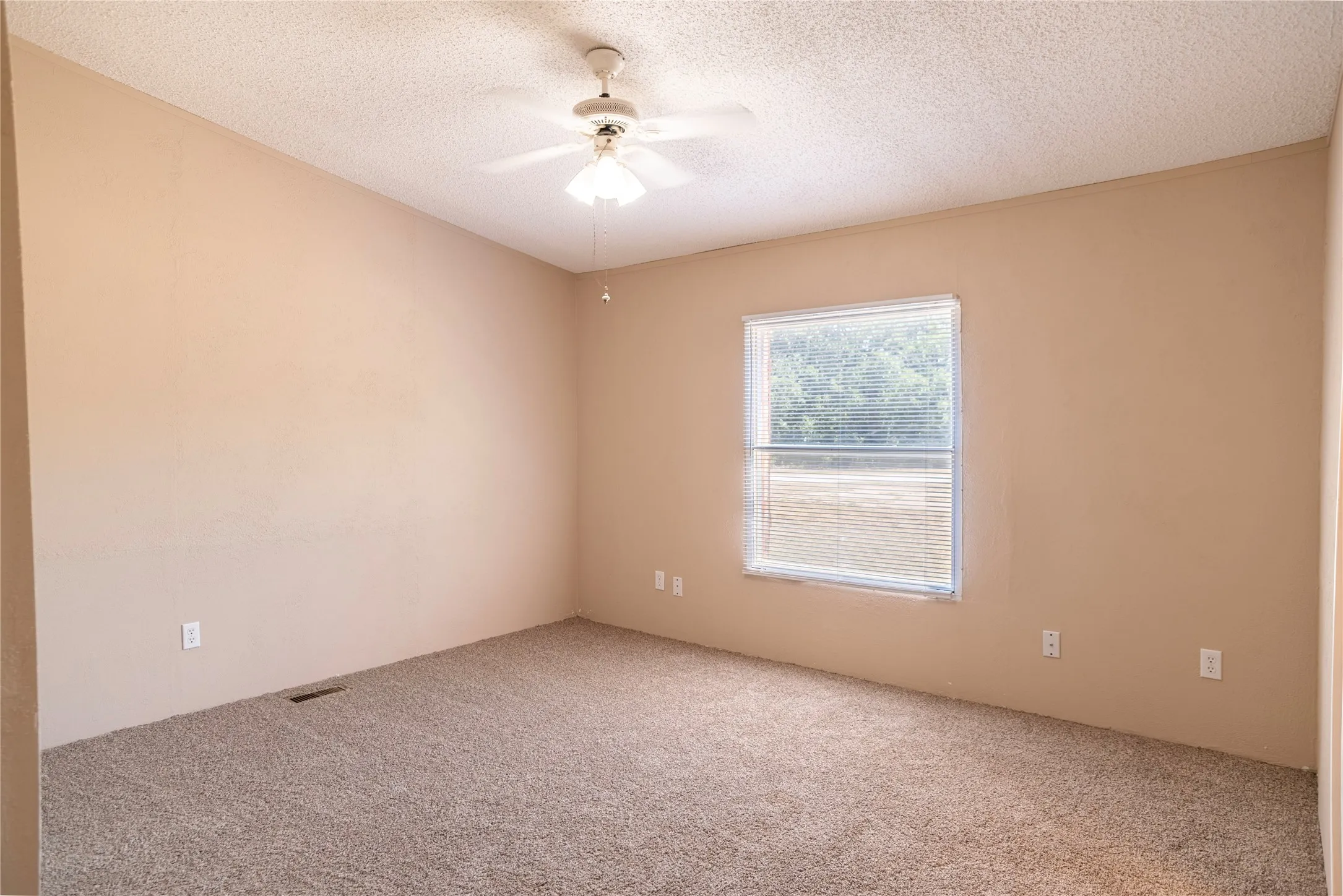 Carpeted interior space featuring a window with integrated blinds, a ceiling fan with lighting, and neutral-toned walls