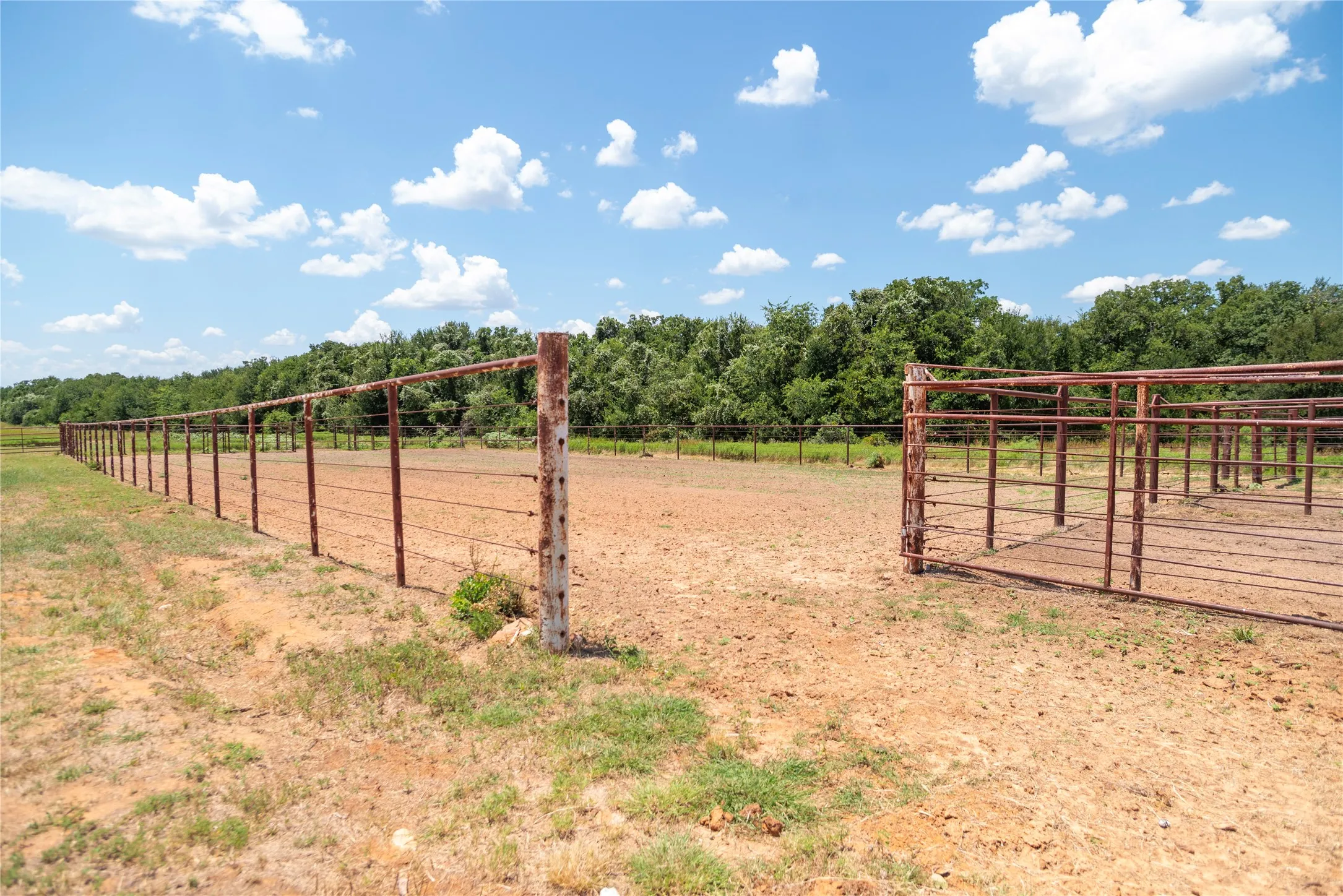 Expansive fenced enclosure featuring a large dirt ground, metal fencing, and a separate pen area