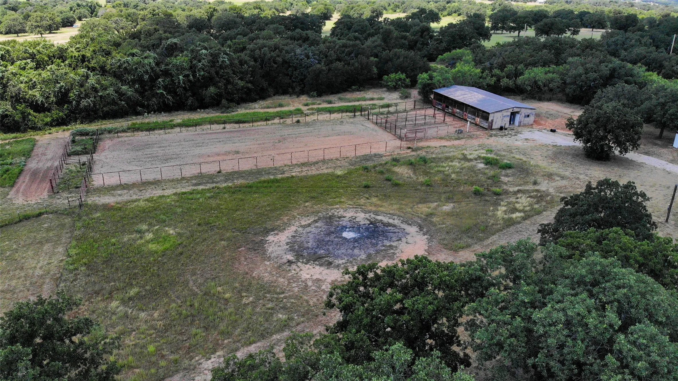 Expansive acreage featuring a fenced riding arena, a large metal-roofed barn, and a circular cleared area