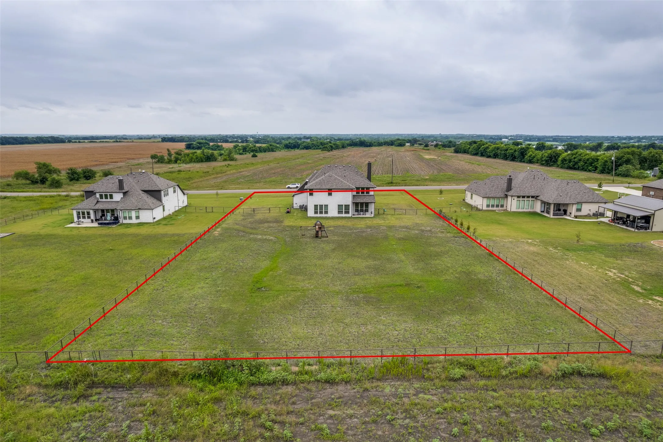 Expansive grass lot featuring a partial wire fence and surrounding open fields