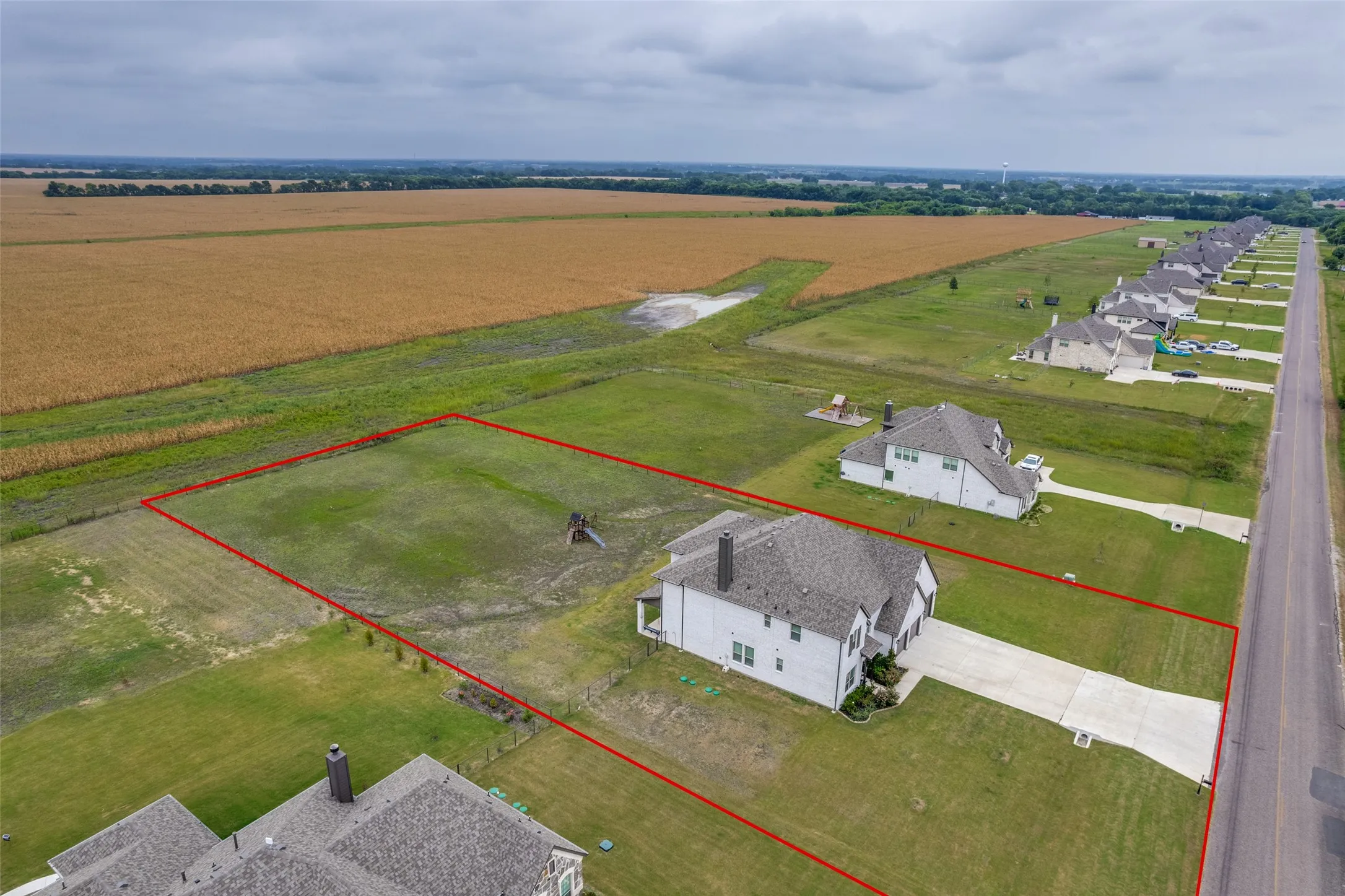 Expansive lot featuring a large grassy area, a concrete driveway, and a residential structure with a gray shingle roof