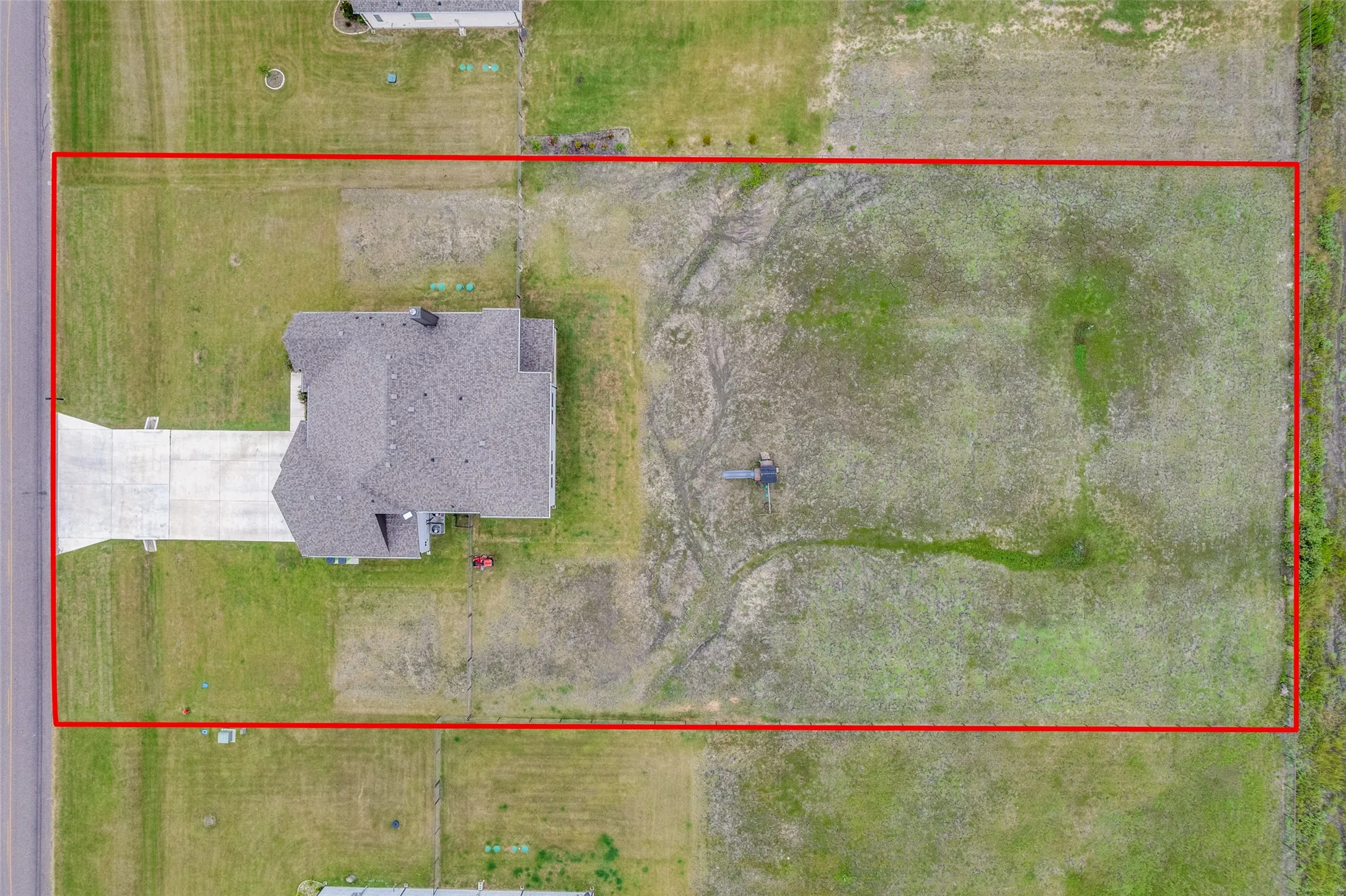 Expansive rectangular lot featuring a single-family residence with a gray shingle roof and a concrete driveway