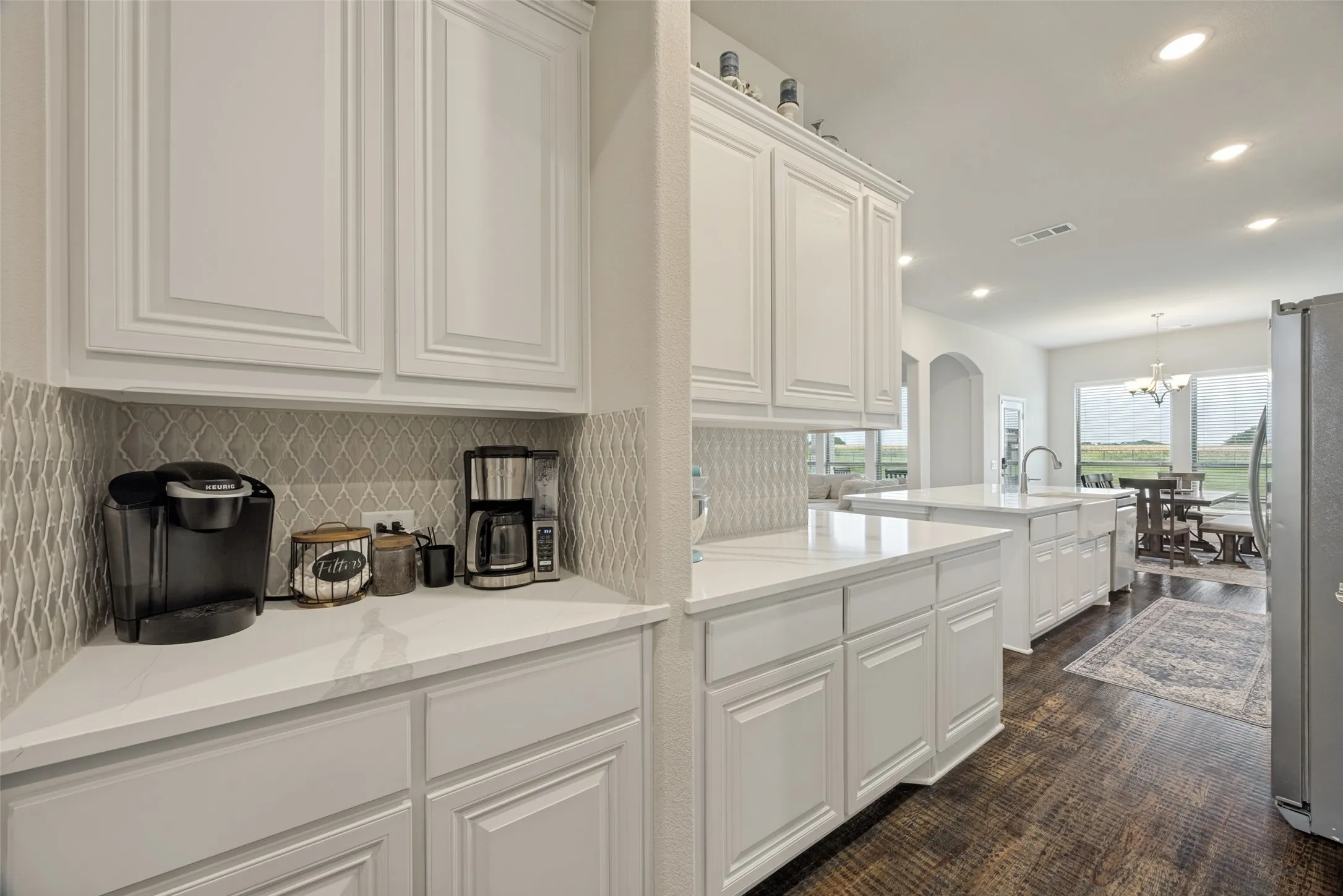 Kitchen featuring white cabinetry, light-toned countertops, a farmhouse-style sink with a gooseneck faucet, a built-in cooktop, and a decorative tile backsplash