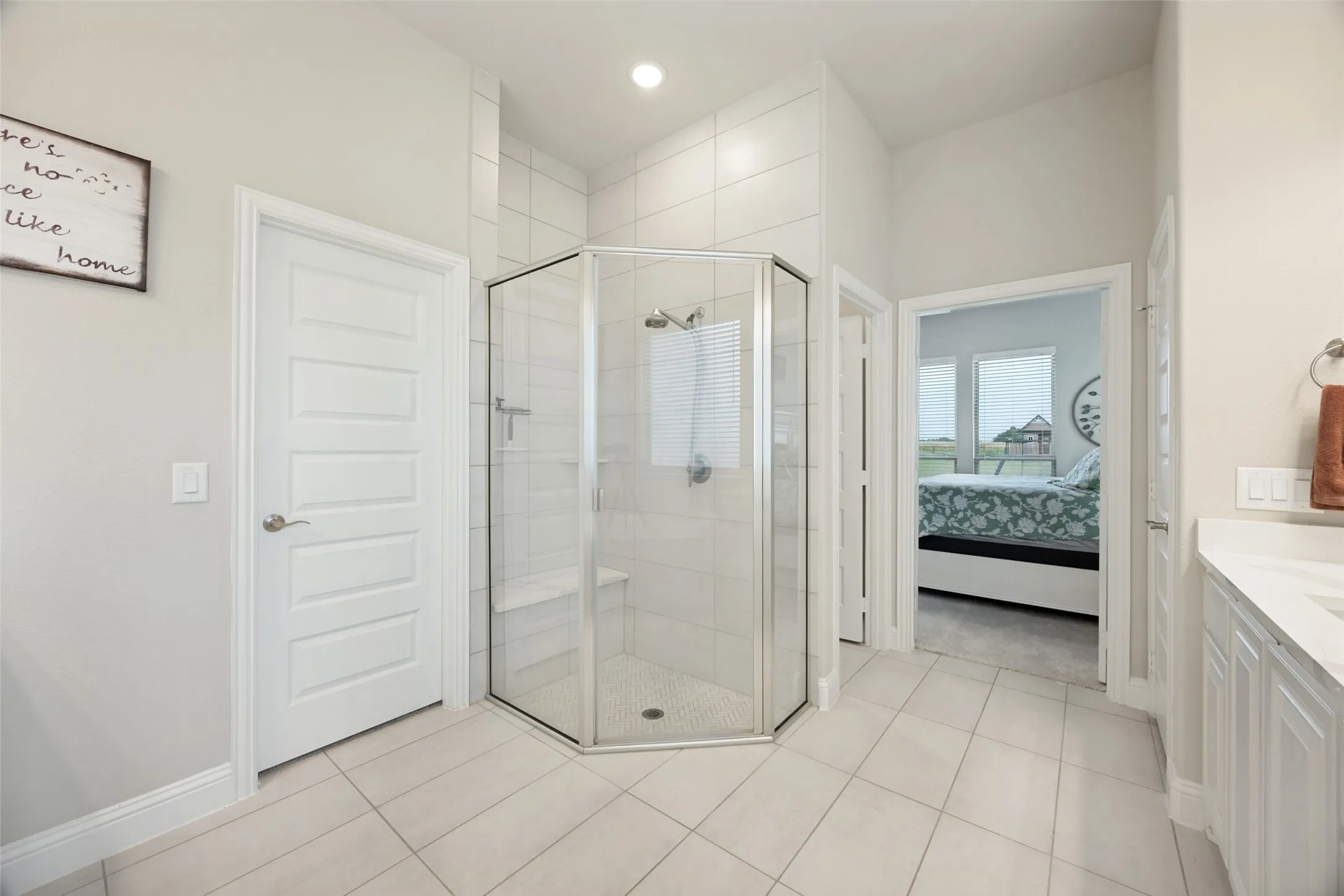 Downstairs primary Bathroom featuring dual vanities with white cabinetry and integrated sinks, a corner garden tub, a glass-enclosed shower, and tile flooring