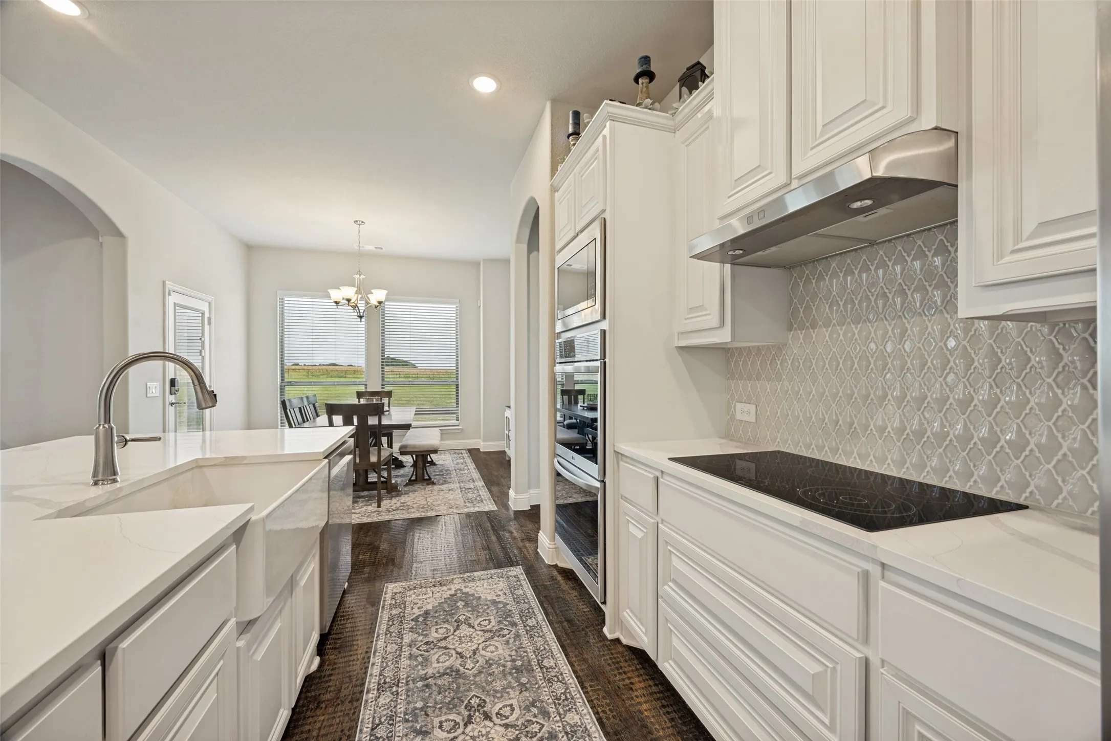 Spacious kitchen featuring an oversized island with countertop seating, white cabinetry, integrated stainless steel appliances, a geometric tile backsplash, and dark wood-finish flooring