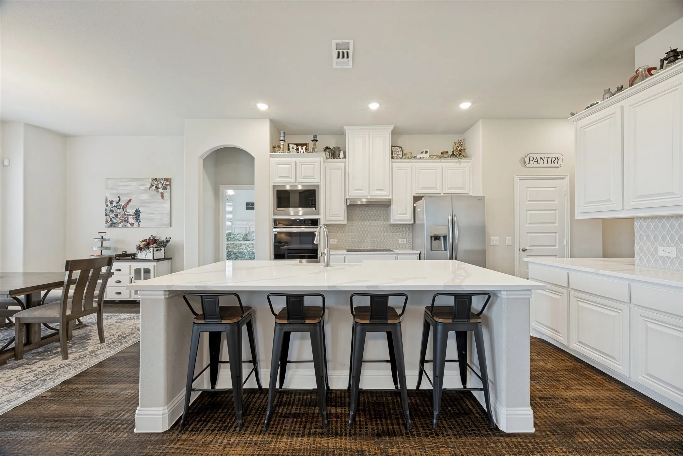 Spacious open-concept living area featuring wood-finish flooring, a stone-clad fireplace with a dark wood mantel, and arched doorways