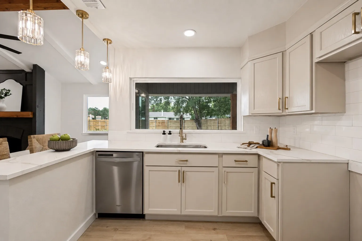 Kitchen featuring light-toned cabinetry with brass hardware, a stainless steel dishwasher, white subway tile backsplash, and light-toned countertops