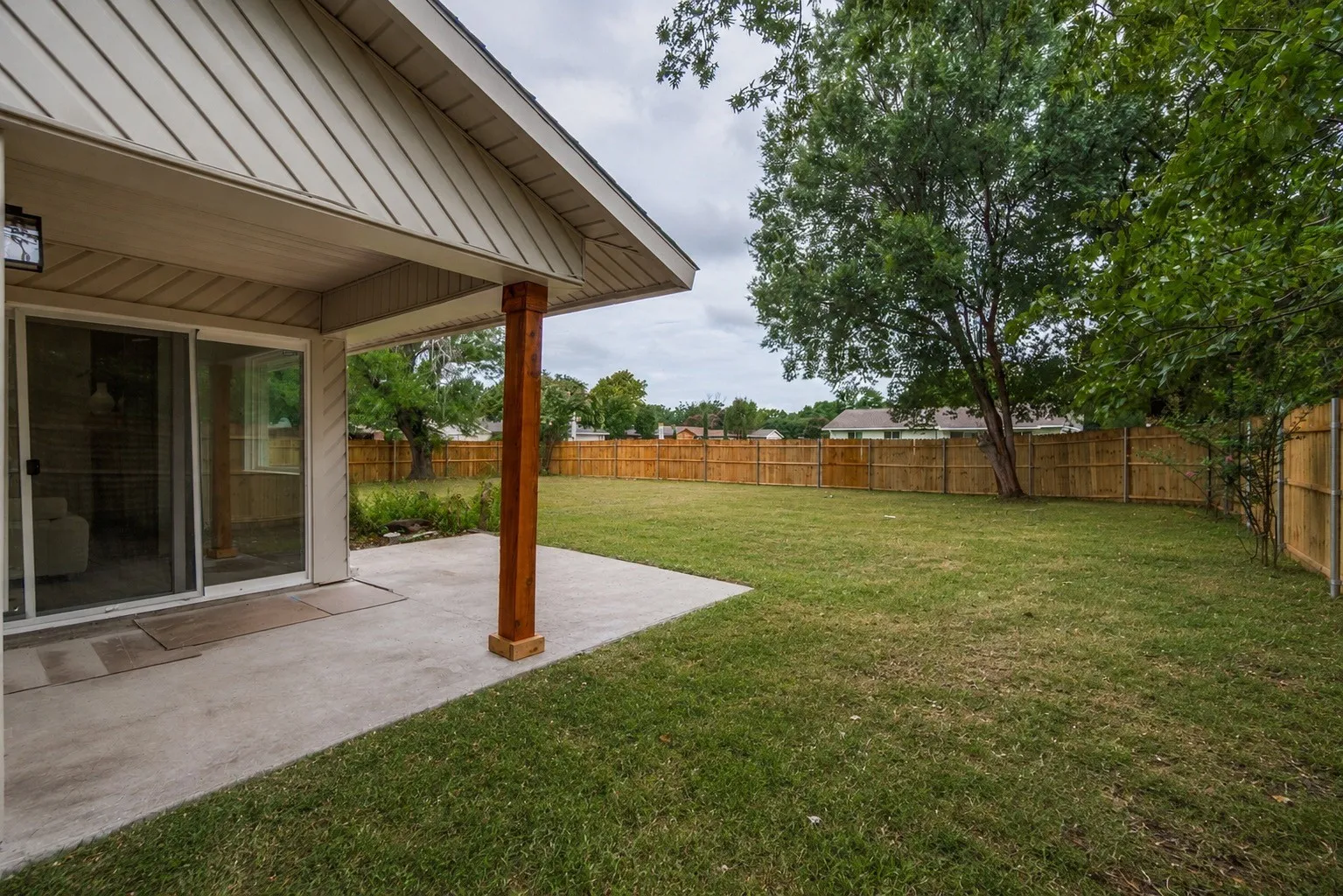 Rear exterior patio with a wood-finished support column, a sliding glass door, and a full wood privacy fence surrounding a grassy yard