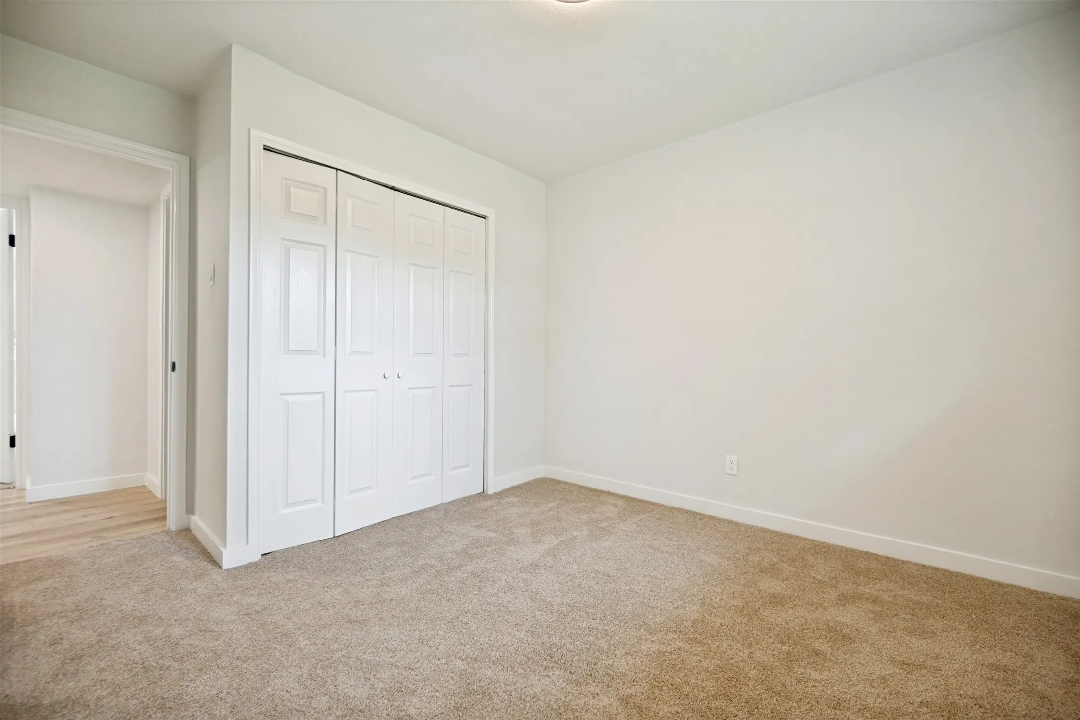 Carpeted room featuring a four-panel bi-fold closet, white walls, and white baseboards