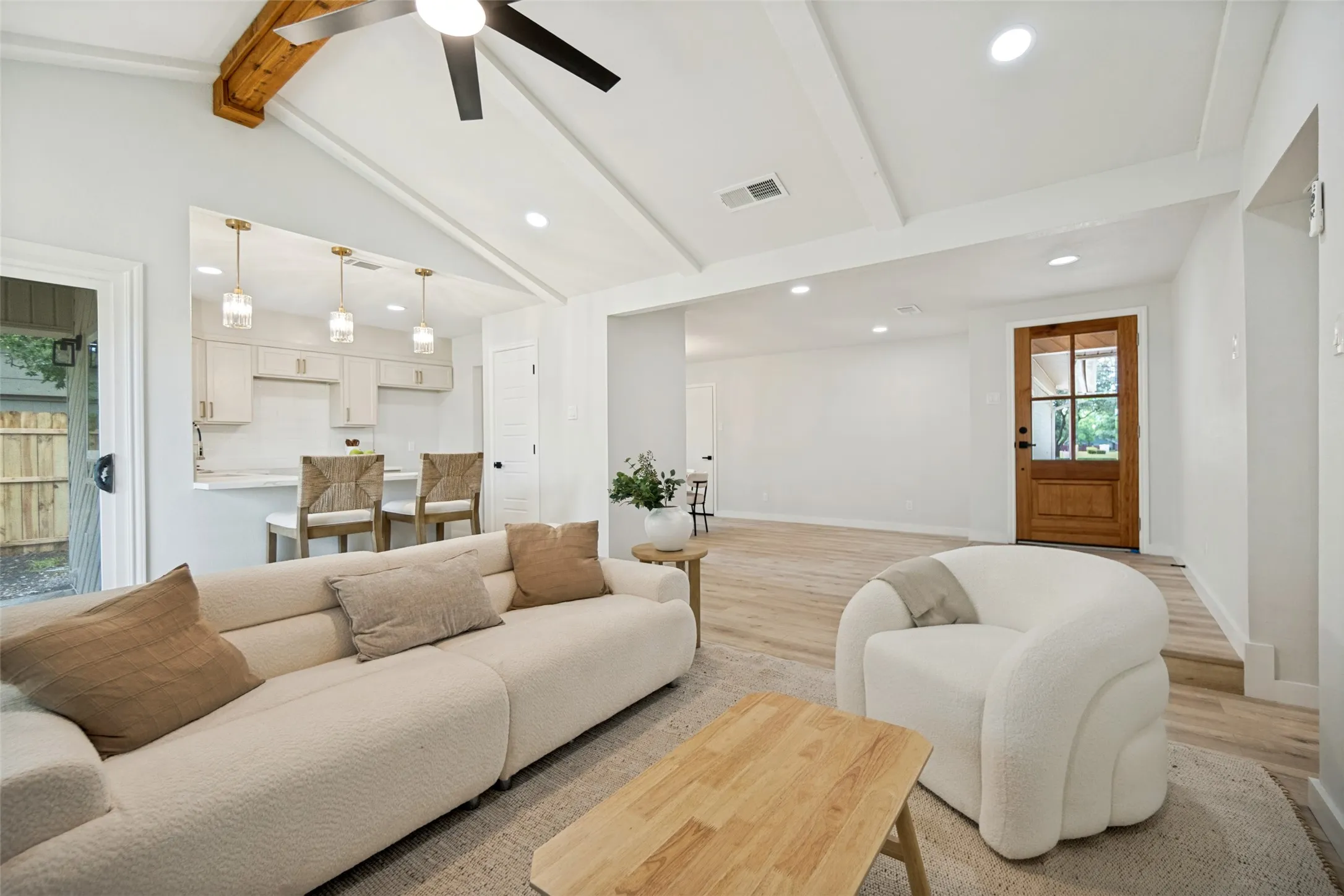 Vaulted ceiling living area with a visible kitchen passthrough, wood-finish flooring, recessed lighting, and a prominent wood-panel front door with glass inserts