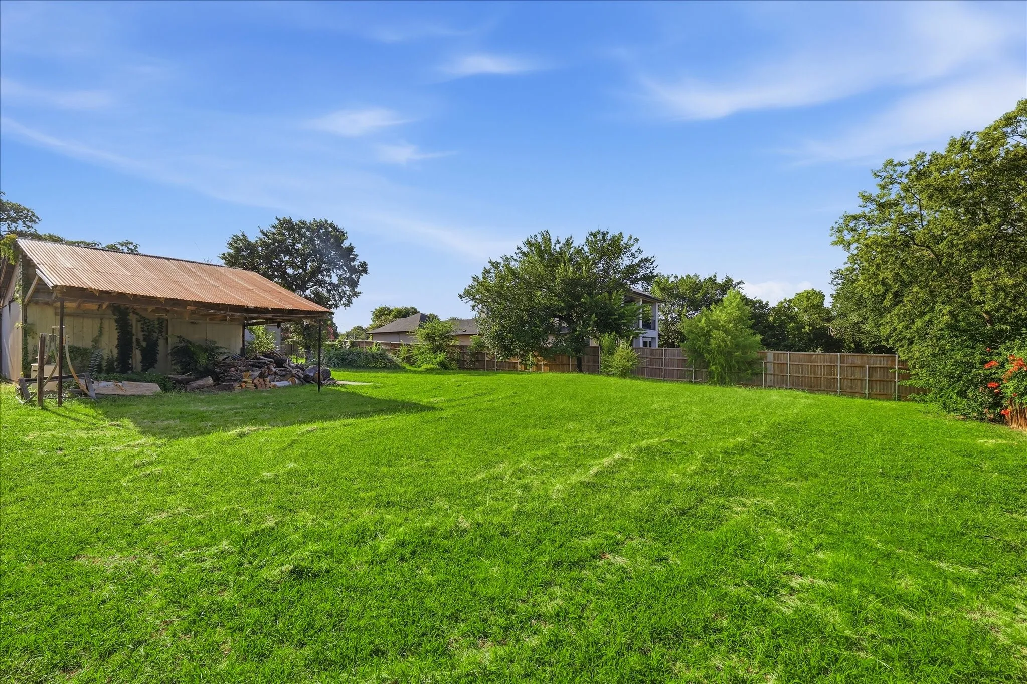 Expansive green lawn with a rustic open-sided shed featuring a corrugated metal roof
