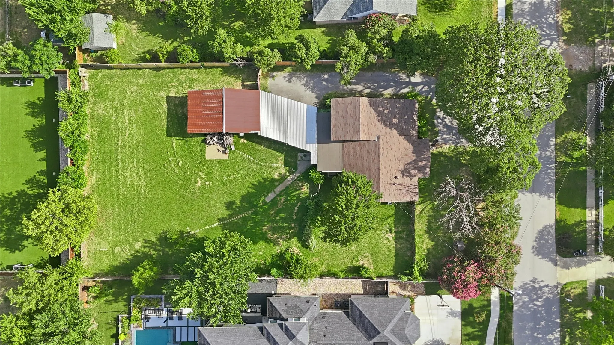 Aerial view showcasing a property with a significant grassy area, an accessory structure featuring a red metal roof, and a covered walkway