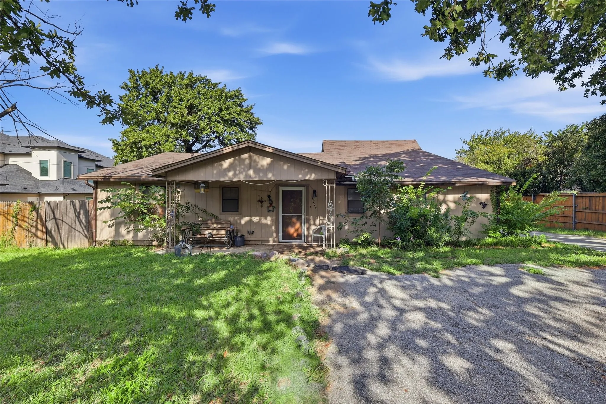 Single-story residence featuring a covered front porch with decorative columns, a gravel driveway, and mature landscaping