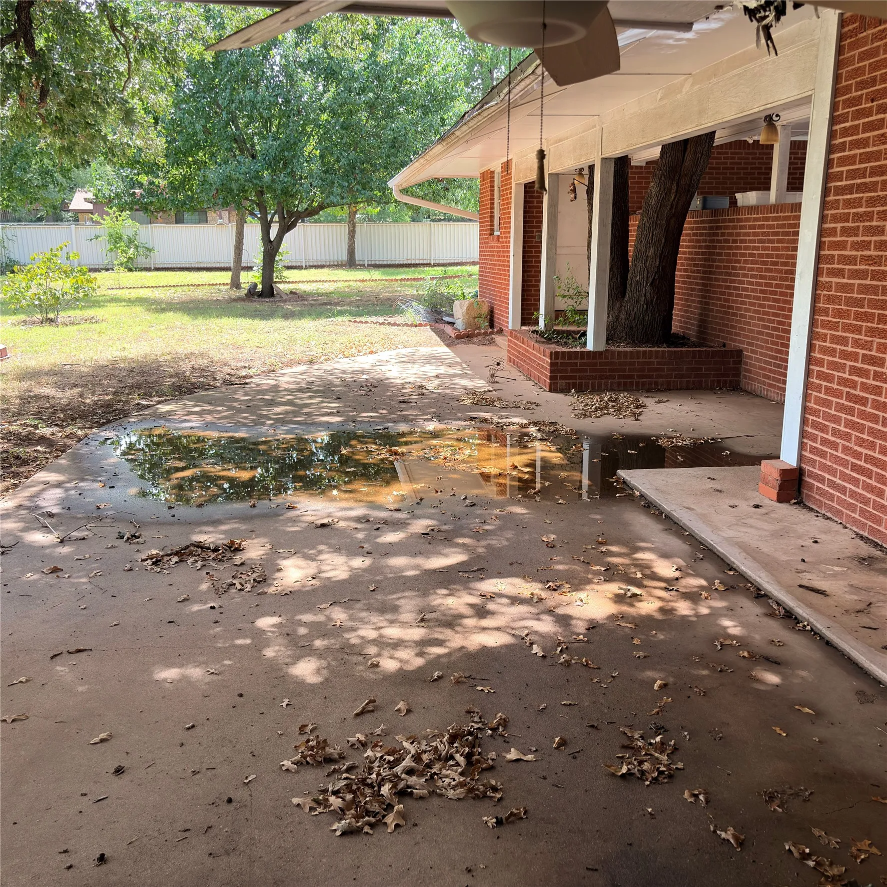 Brick exterior featuring a covered patio, concrete flooring, and a built-in planter with an established tree