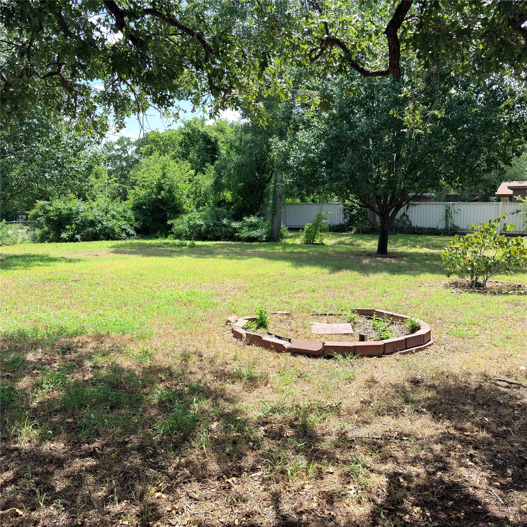 Expansive outdoor space featuring mature trees, a manicured lawn, and a brick-edged planting bed