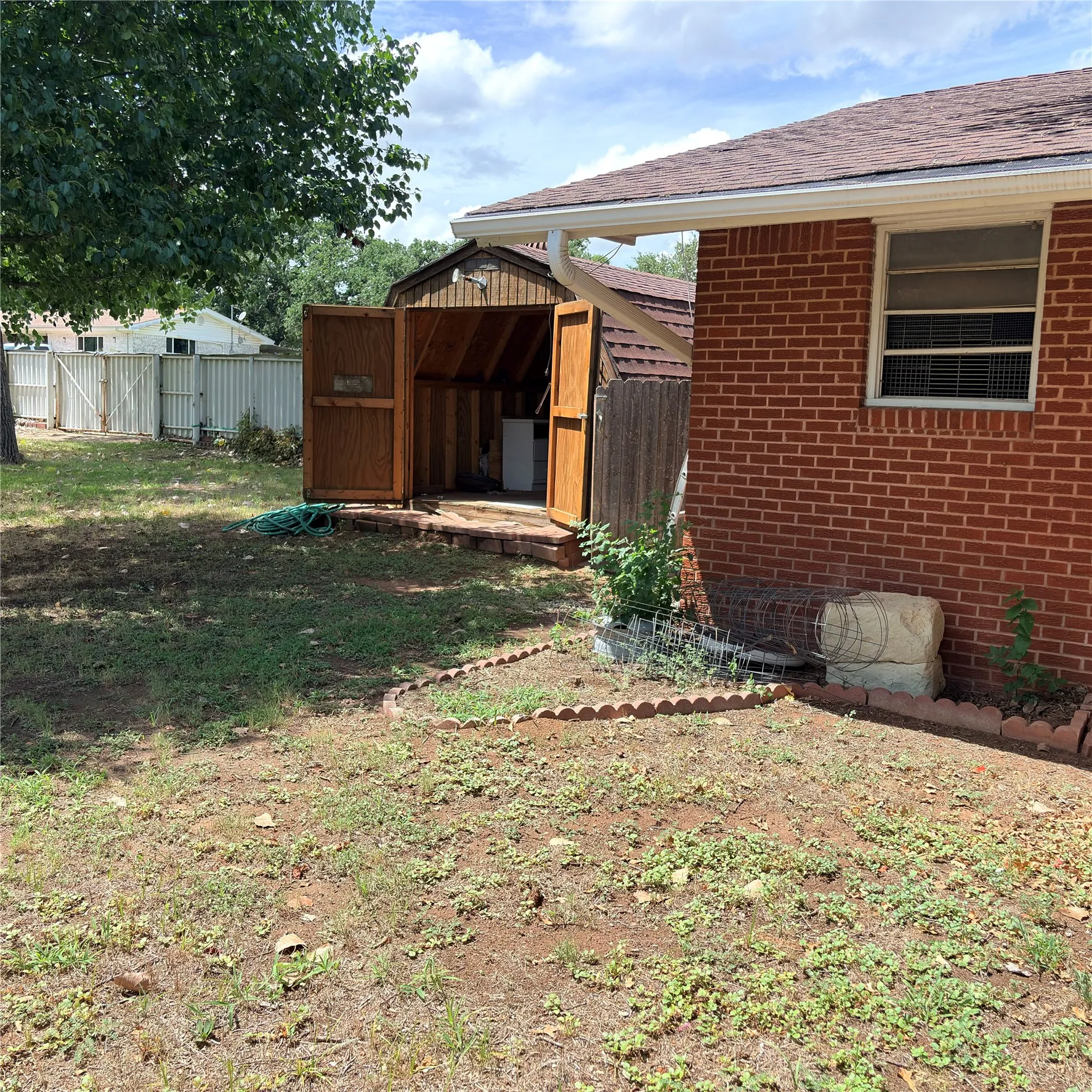 Backyard featuring a red brick exterior, a wood-sided storage shed with double doors, and a partial privacy fence