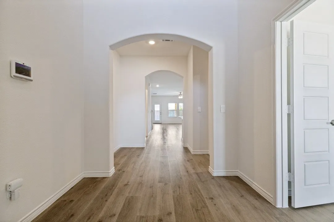 Hallway featuring wood-finish flooring, an arched entryway, recessed lighting, white baseboards, and a modern door with square paneling