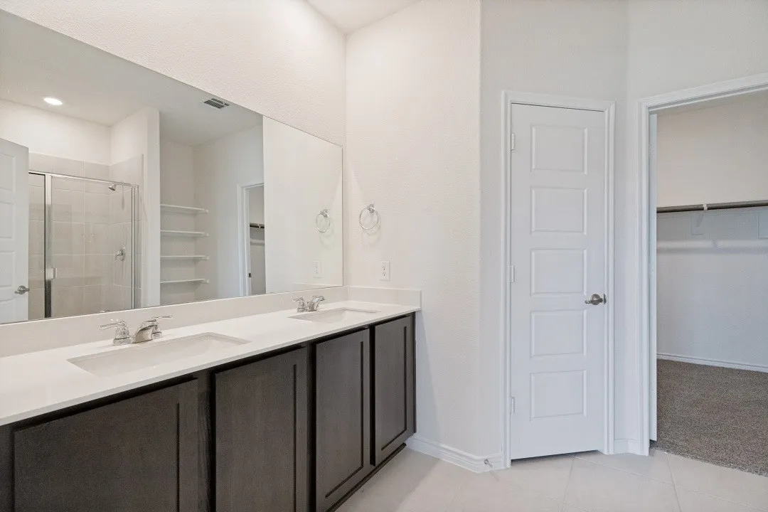 Bathroom featuring a dual vanity with undermount sinks, white countertops, dark wood cabinetry, a large wall-mounted mirror, and tile flooring