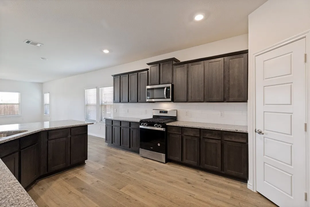 Modern kitchen featuring dark wood-finish cabinetry, light-colored speckled countertops, a stainless steel gas range, and a built-in microwave