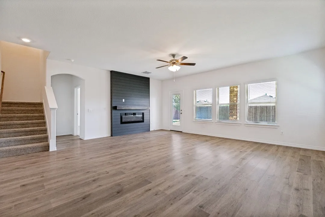 Spacious living area featuring wood-finish flooring, a modern black shiplap fireplace with mantel, and a ceiling fan