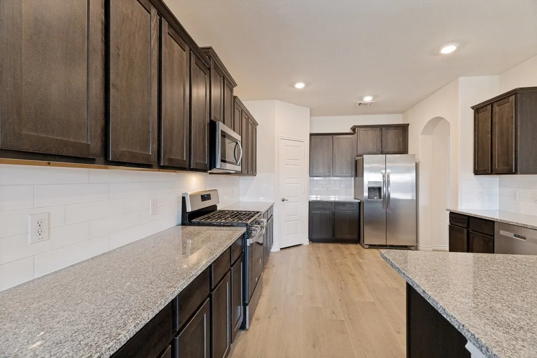 Kitchen featuring dark wood-finish cabinetry, light speckled countertops, stainless steel appliances, a white subway tile backsplash, and light wood-finish flooring