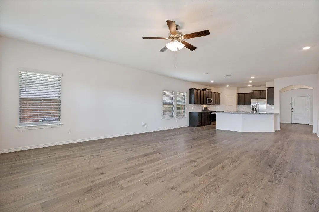 Expansive open-concept living area featuring wood-finish flooring, a ceiling fan with integrated lighting, and recessed ceiling lighting