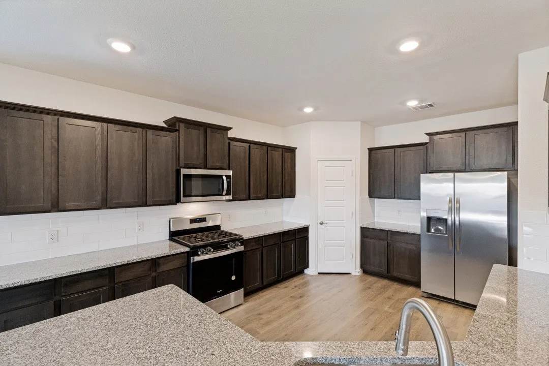 Kitchen featuring dark wood cabinetry, light-toned countertops, stainless steel appliances, a subway tile backsplash, and recessed lighting