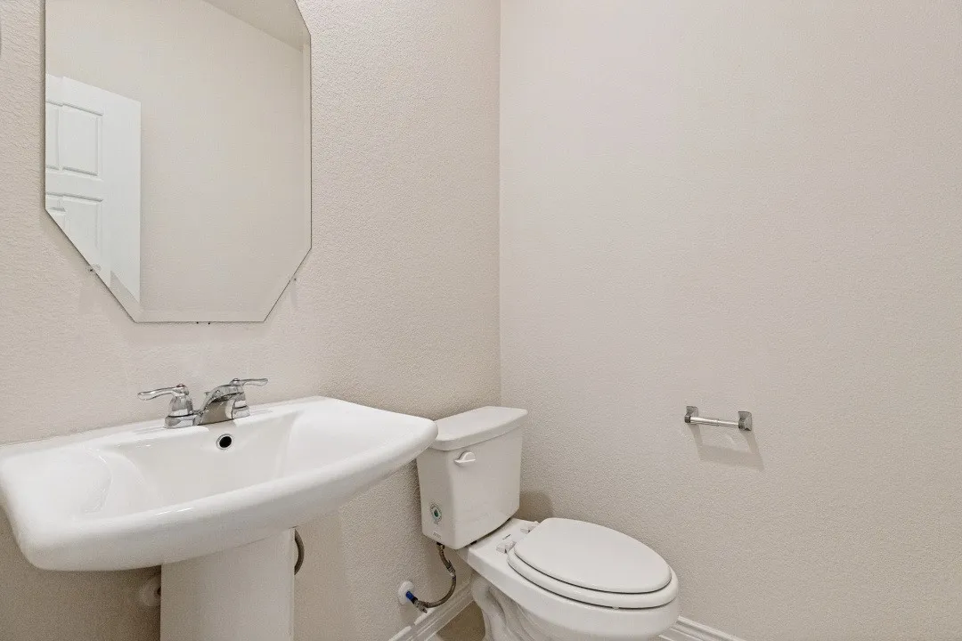 Pedestal sink with chrome faucet, octagonal frameless mirror, and white toilet