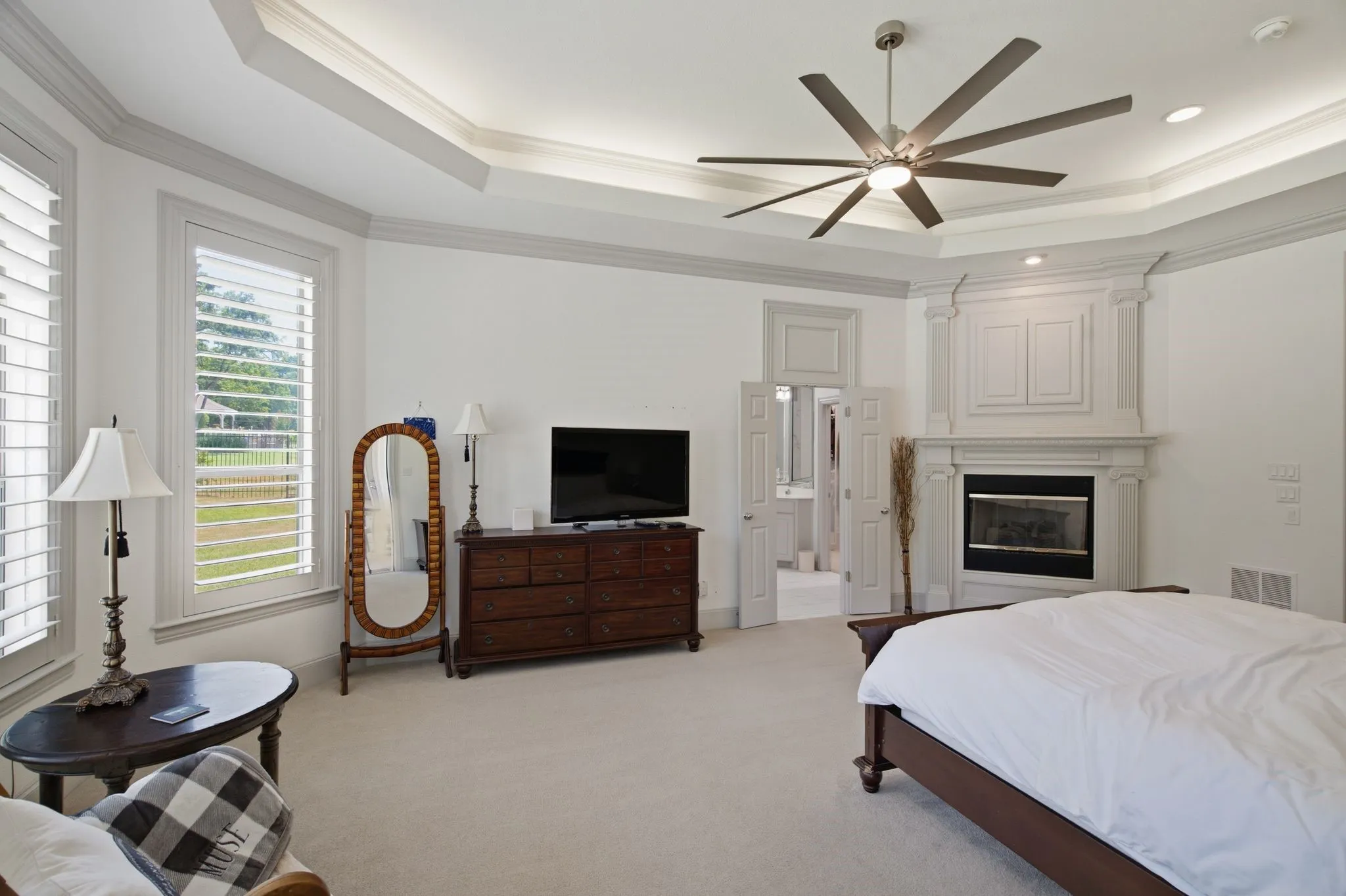 Spacious room featuring a tray ceiling with recessed lighting, a multi-blade ceiling fan, and a fireplace with an ornate mantel