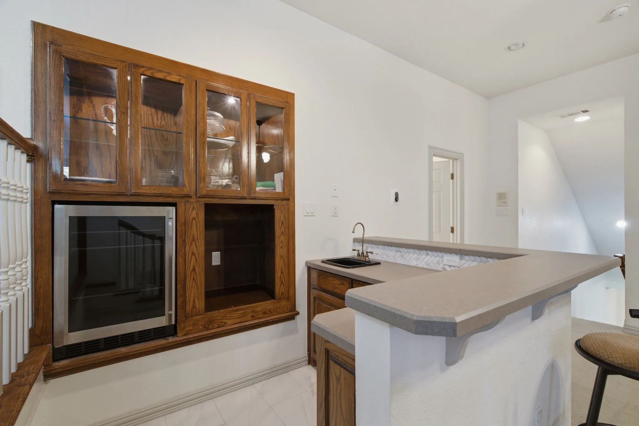 Built-in wet bar featuring wood cabinetry, glass-front upper cabinets, and a beverage refrigerator